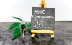 The HHC cartridge stands next to a chalkboard with the text HHC Hexahydrocannabinol and a representation of the chemical structure